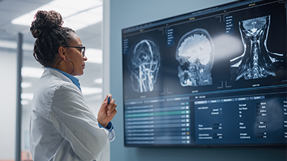 A woman in a lab coat looks at medical images on a screen