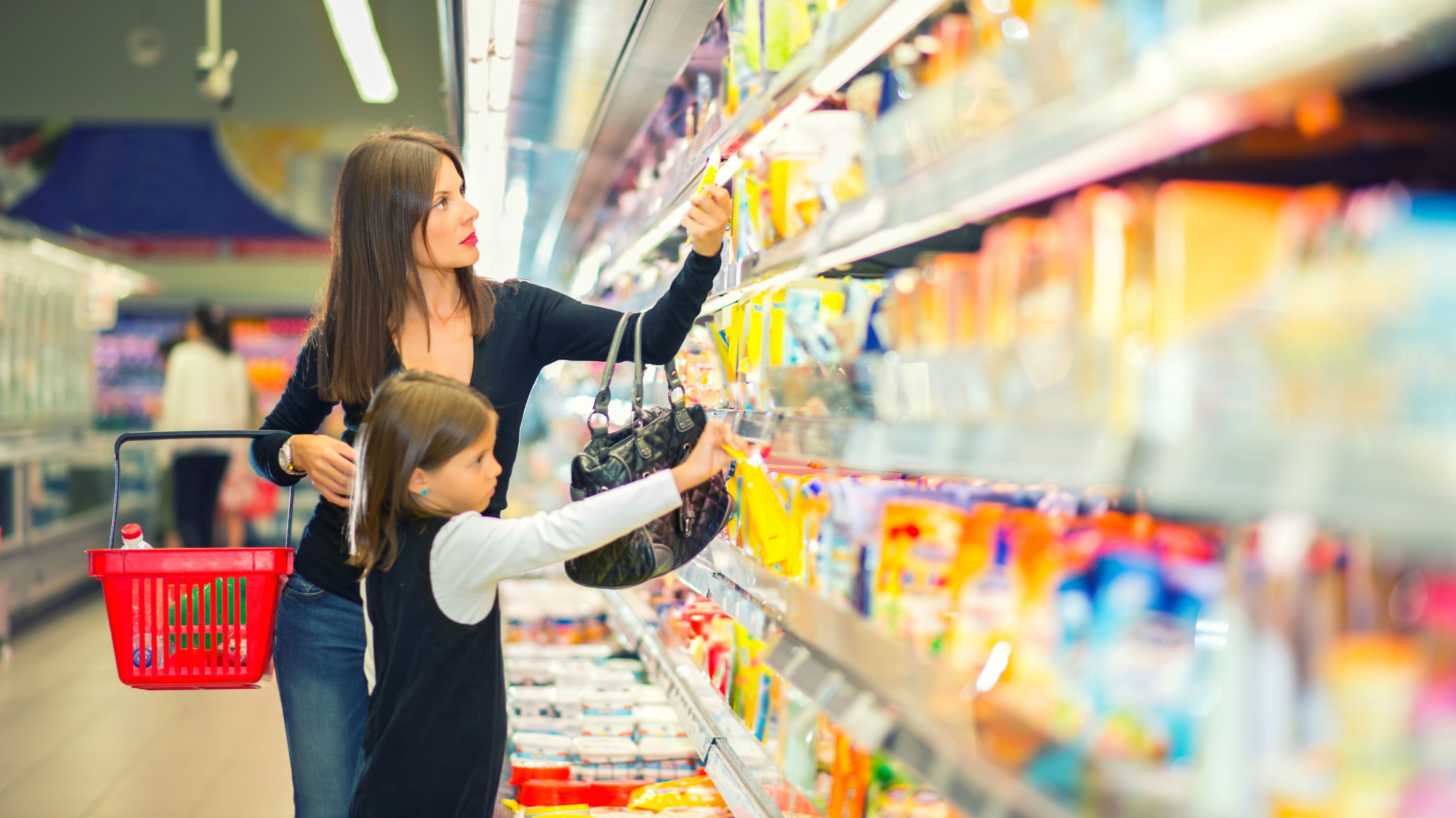 Mom and young daughter shopping in dairy aisle of supermarket. 