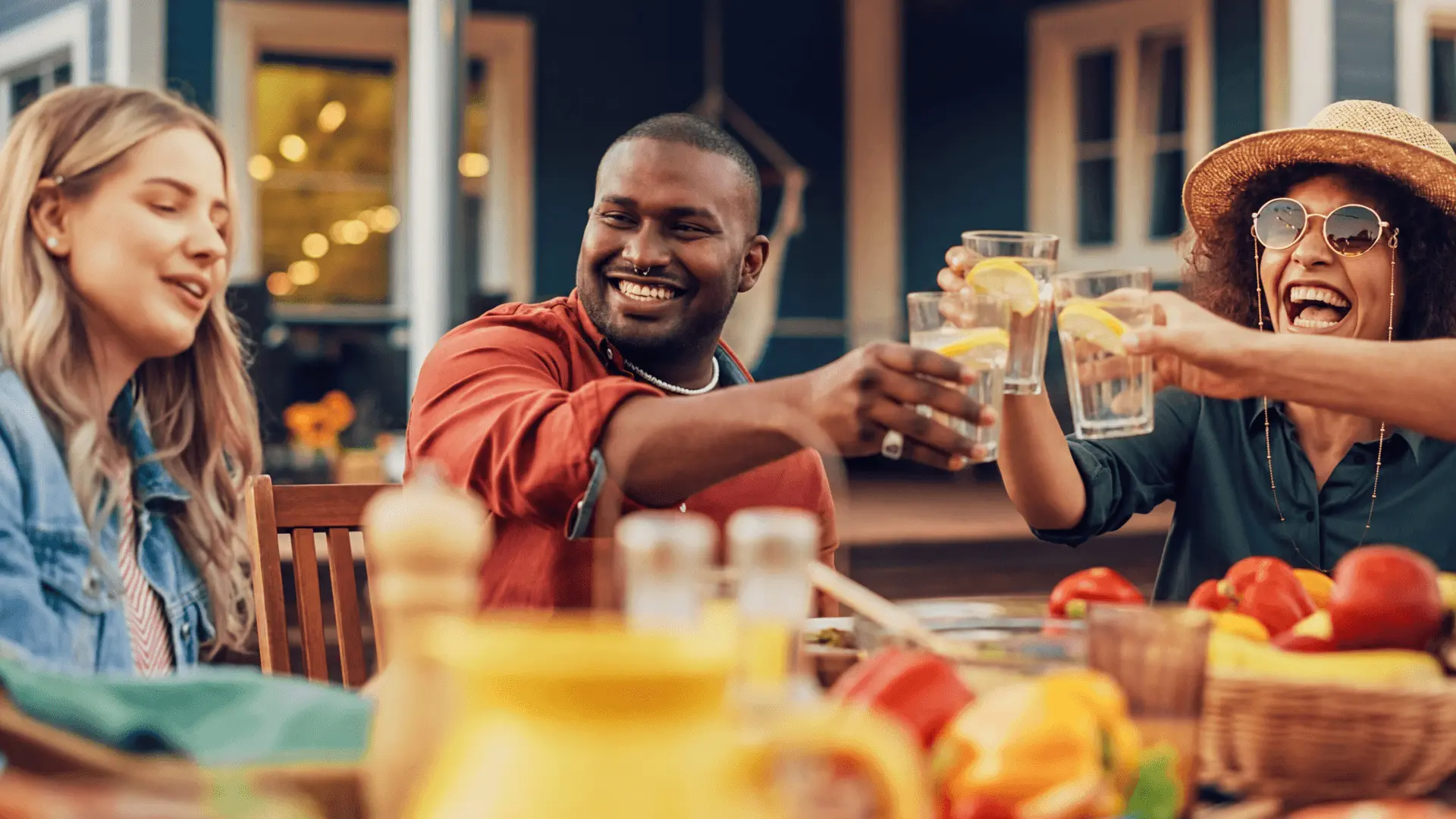 People toasting glasses of water with lemon at an outdoor table.