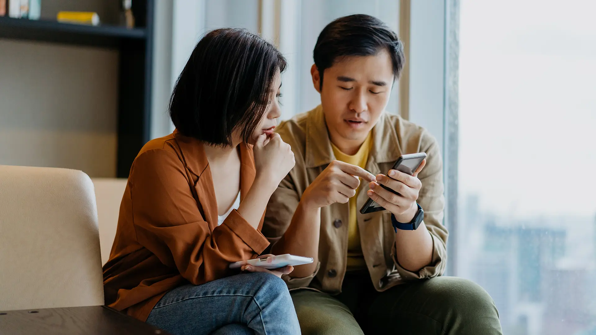 Two people sitting on the sofa looking at smartphones.
