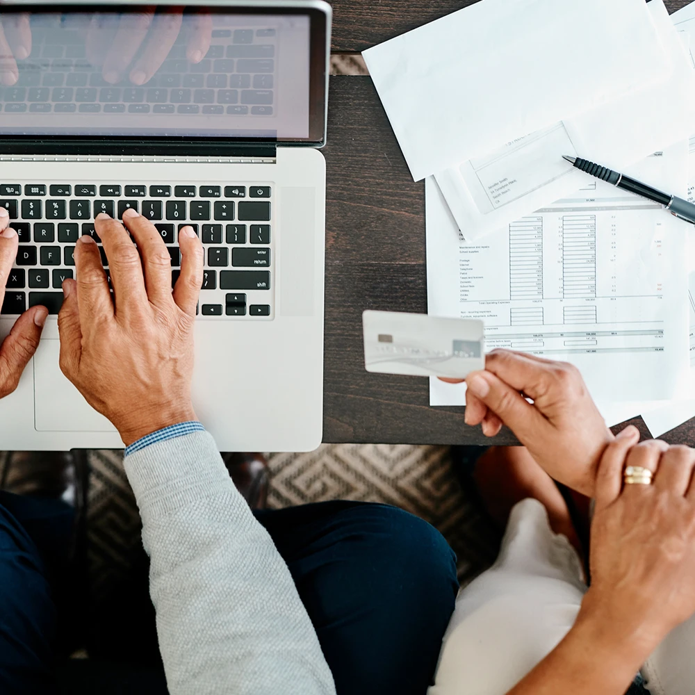 Two sets of hands working at a computer with paperwork.