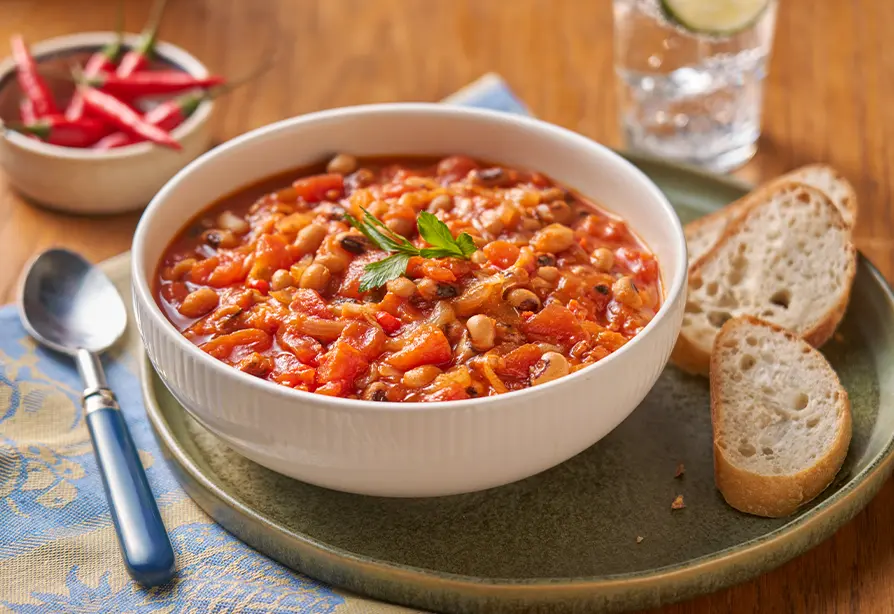 Bean and vegetable stew in a white bowl with bread slices. 