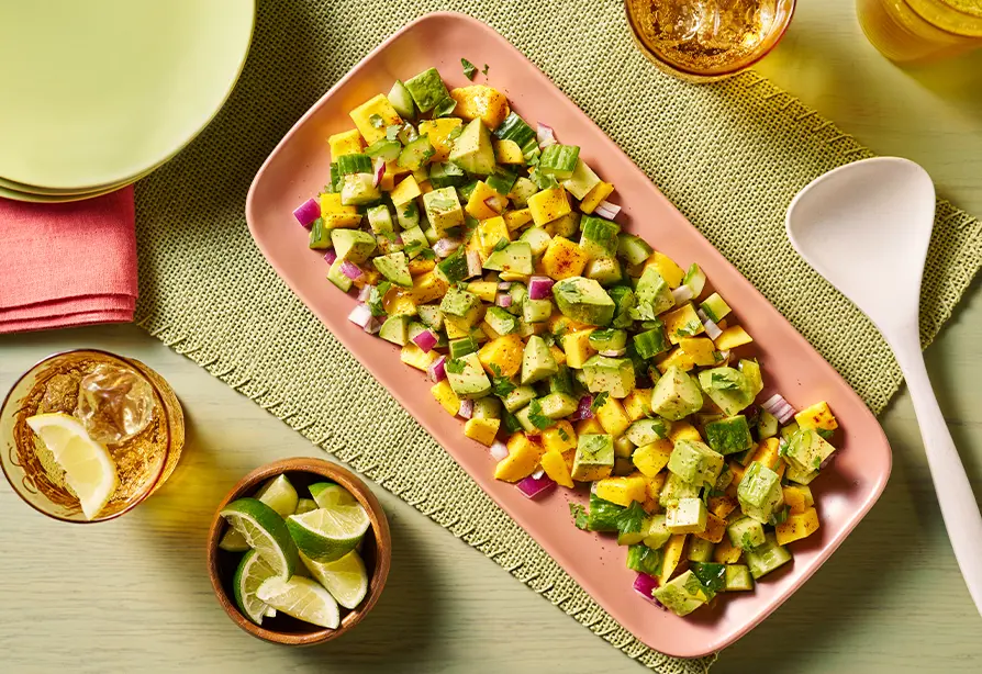 Mango, avocado, cucumber and onion salad on a pink serving platter. 
