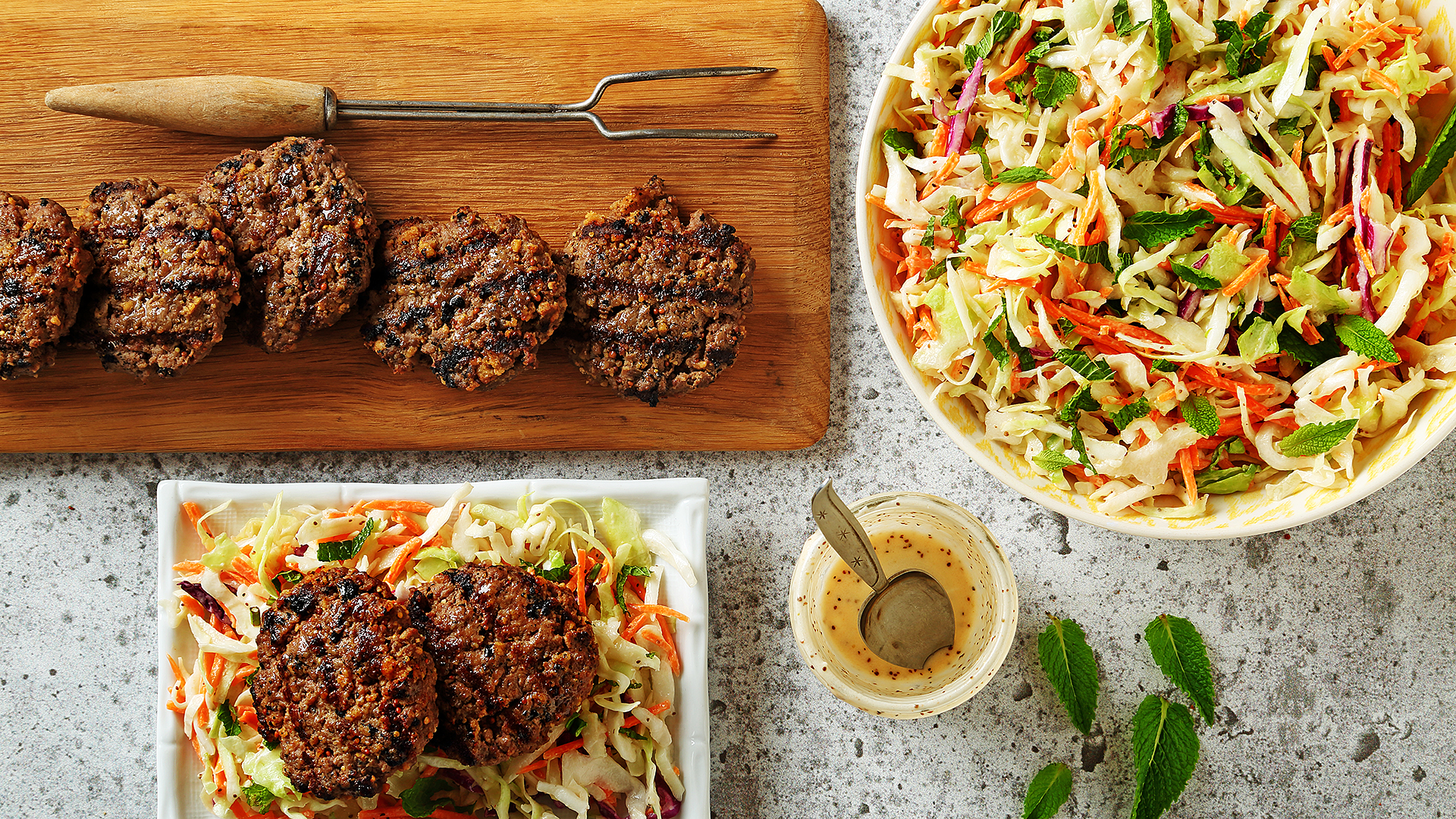 Slaw salad in a big serving bowl with sliders on a wooden cutting board and an assembled salad. 