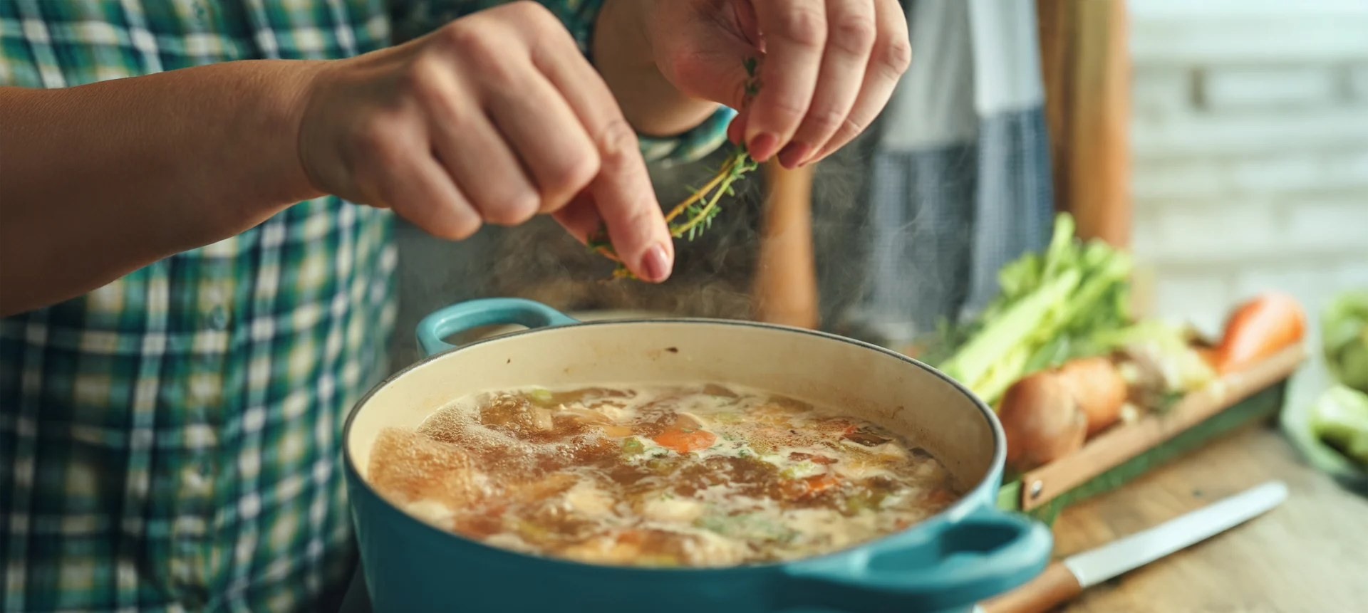 Woman seasoning a pot of homemade soup with fresh herbs.