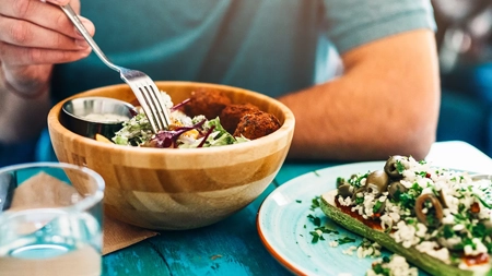 Person eating a salad at a table with an open-faced sandwich.