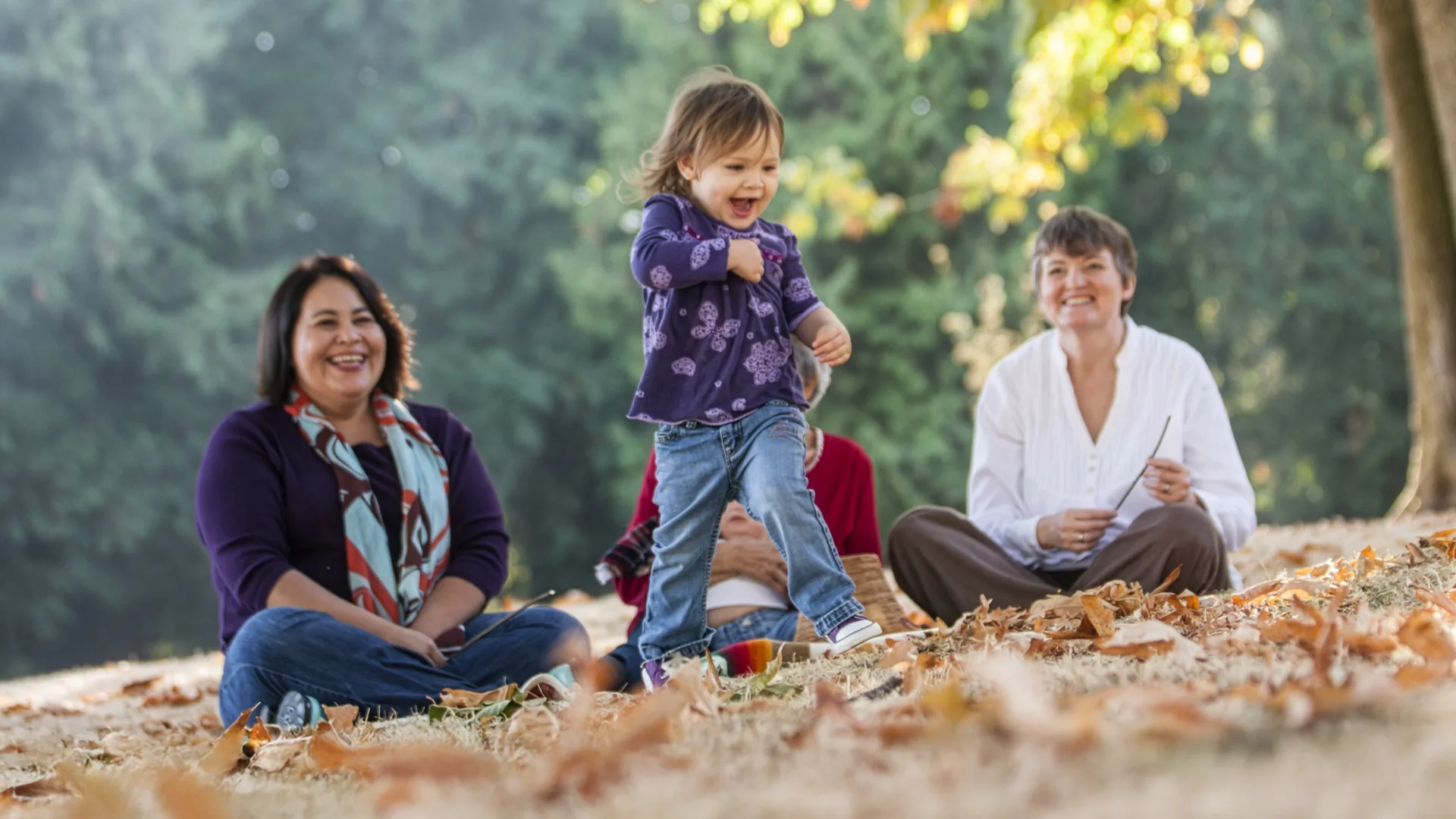 A group sitting outdoors in a park with a child playing 