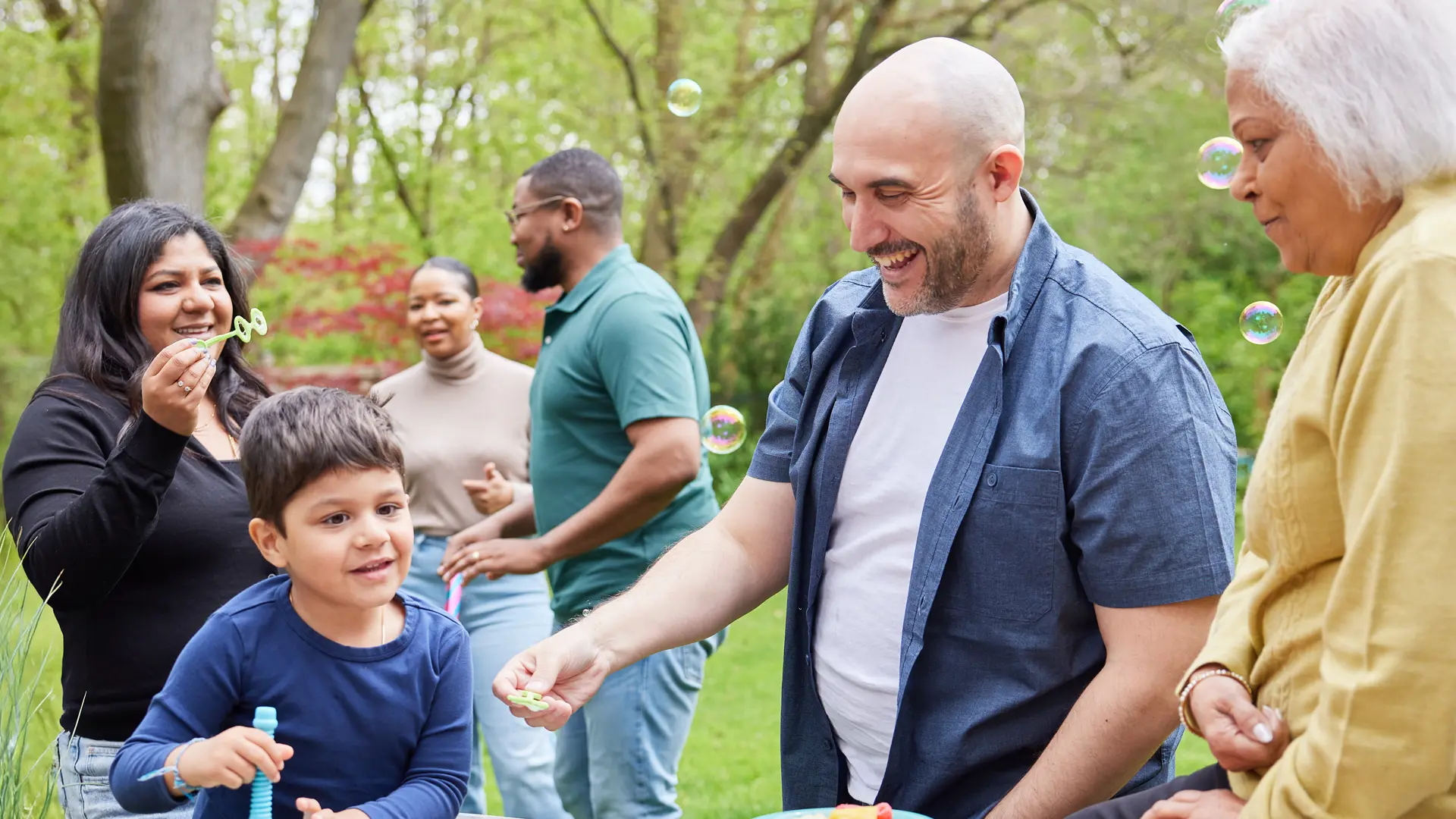 A group of adults and children blow bubbles together outside in a park. 