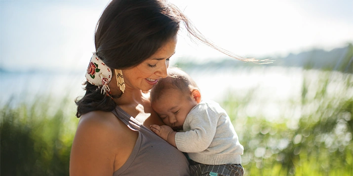 An Indigenous woman holds her sleeping baby while outdoors.