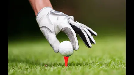A hand wearing a golfing glove placing a ball on a tee.