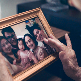 Elderly hand holding a framed photo of a smiling family.
