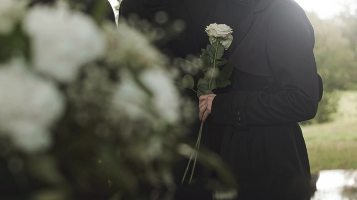 Person holding a single white rose at an outdoor memorial.