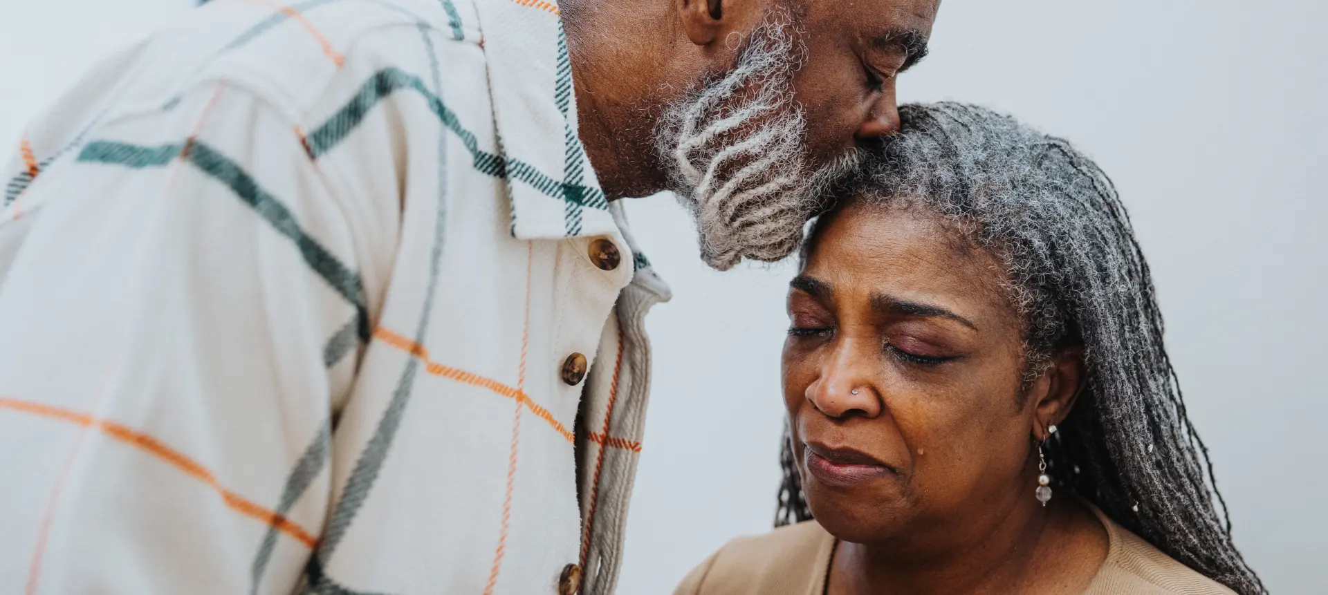 An older couple standing close together, leaning toward each other in a quiet, supportive moment.