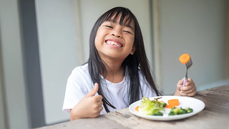 A grinning girl eating a well balanced meal.