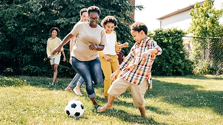 A group of children and adults playing soccer together on a sunny backyard lawn. 