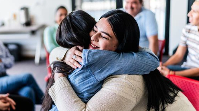 Two people hugging, with others seated in the background. 