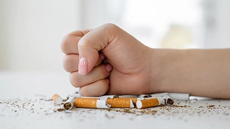 A hand clenches into a fist over broken cigarettes on a table. 