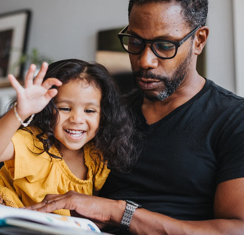 A man sitting with his young daughter reading a book.