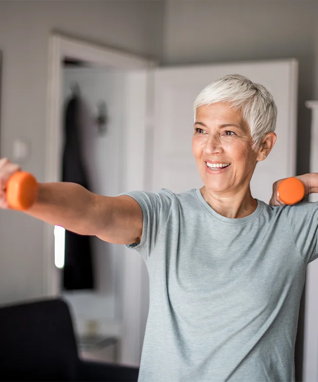 A happy senior woman exercising at home with dumbbells.