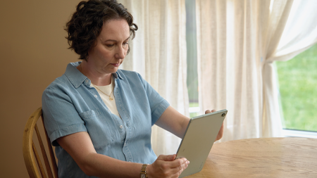 Adria Scarano, sitting at a table, holding a tablet in her hand. 