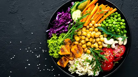 A large bowl on a dark background filled with vegetables including chickpeas, carrots, cabbage and tomatoes.