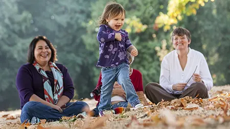 A group sitting outdoors in a park with a child playing.