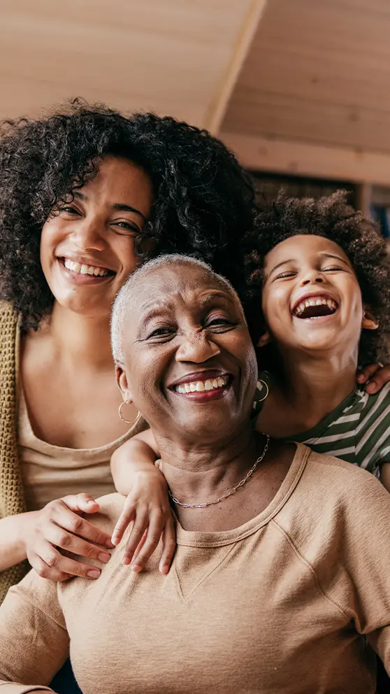 A grandmother, mother and granddaughter smiling and laughing together.