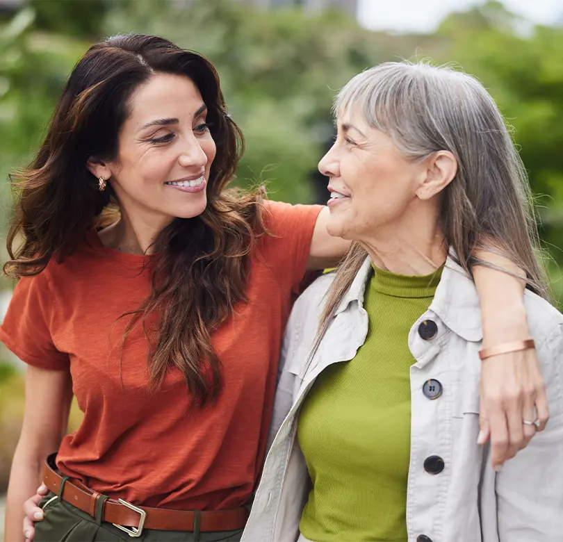 A young woman with her arm around an older woman, smiling and walking together.