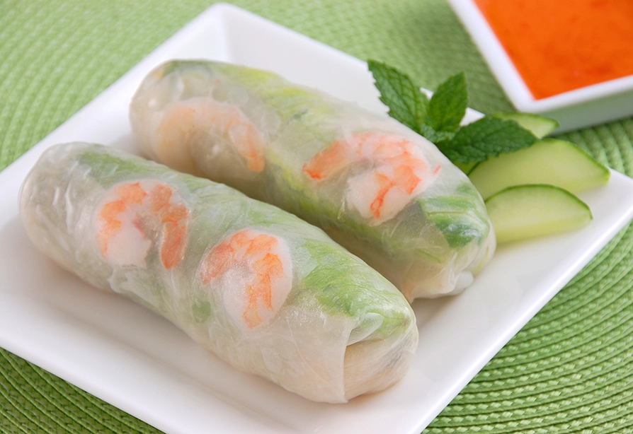 Two Cold shrimp rolls served on a white plate with cucumber slices and mint.