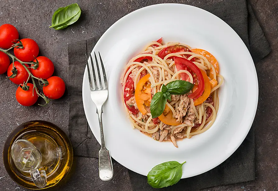 A plate of spaghetti and tuna with pepper and tomatoes.