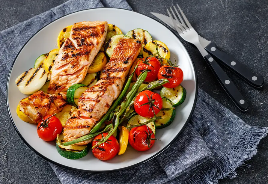 Grilled salmon served on a bed of vegetables on a white plate.