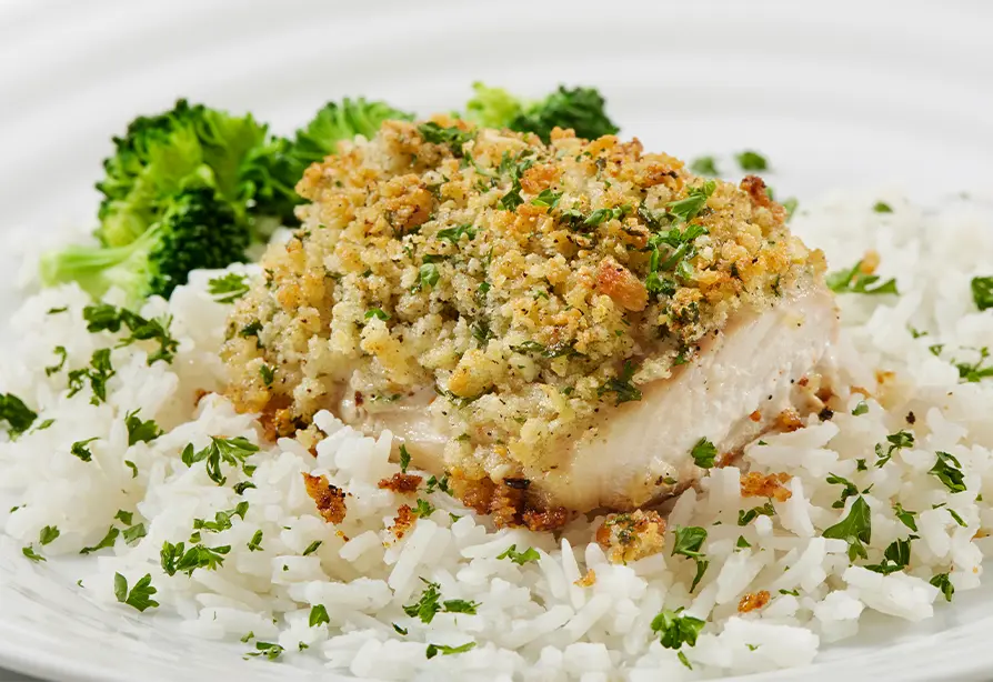 Almond-crusted fish served over broccoli rice on a white plate.
