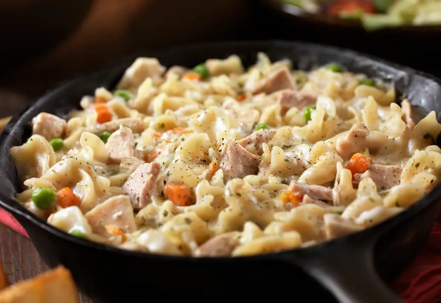 A pan with cooked pasta, tuna, green peas and carrots.