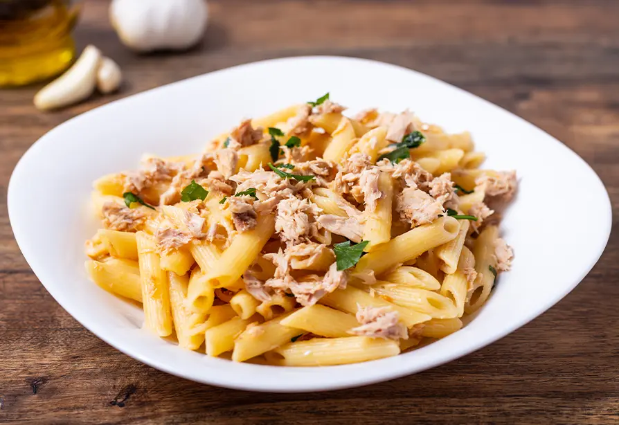 Penne topped with flaked tuna served in a white bowl