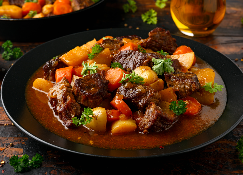 Beef stew with potatoes and vegetables in a black bowl. 