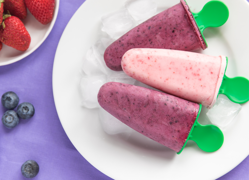Three berry yogurt popsicles on a white plate. 