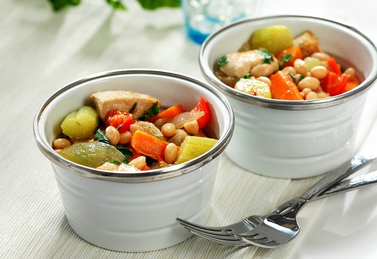Two white bowls filled with cooked chicken, celery, carrots, navy beans and broth