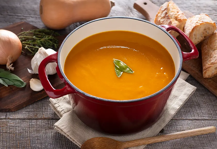Red pot of creamy orange soup with green leaf garnish. 