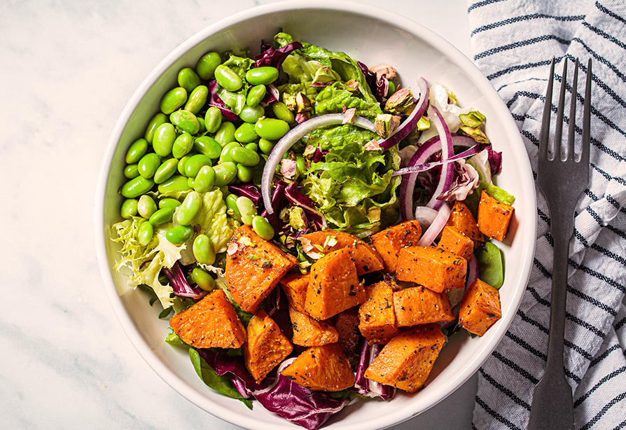 A bowl of salad with edamame, mixed greens, red onion and sweet potato chunks. 