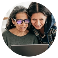 A mother and daughter hunched together to look at a computer screen.