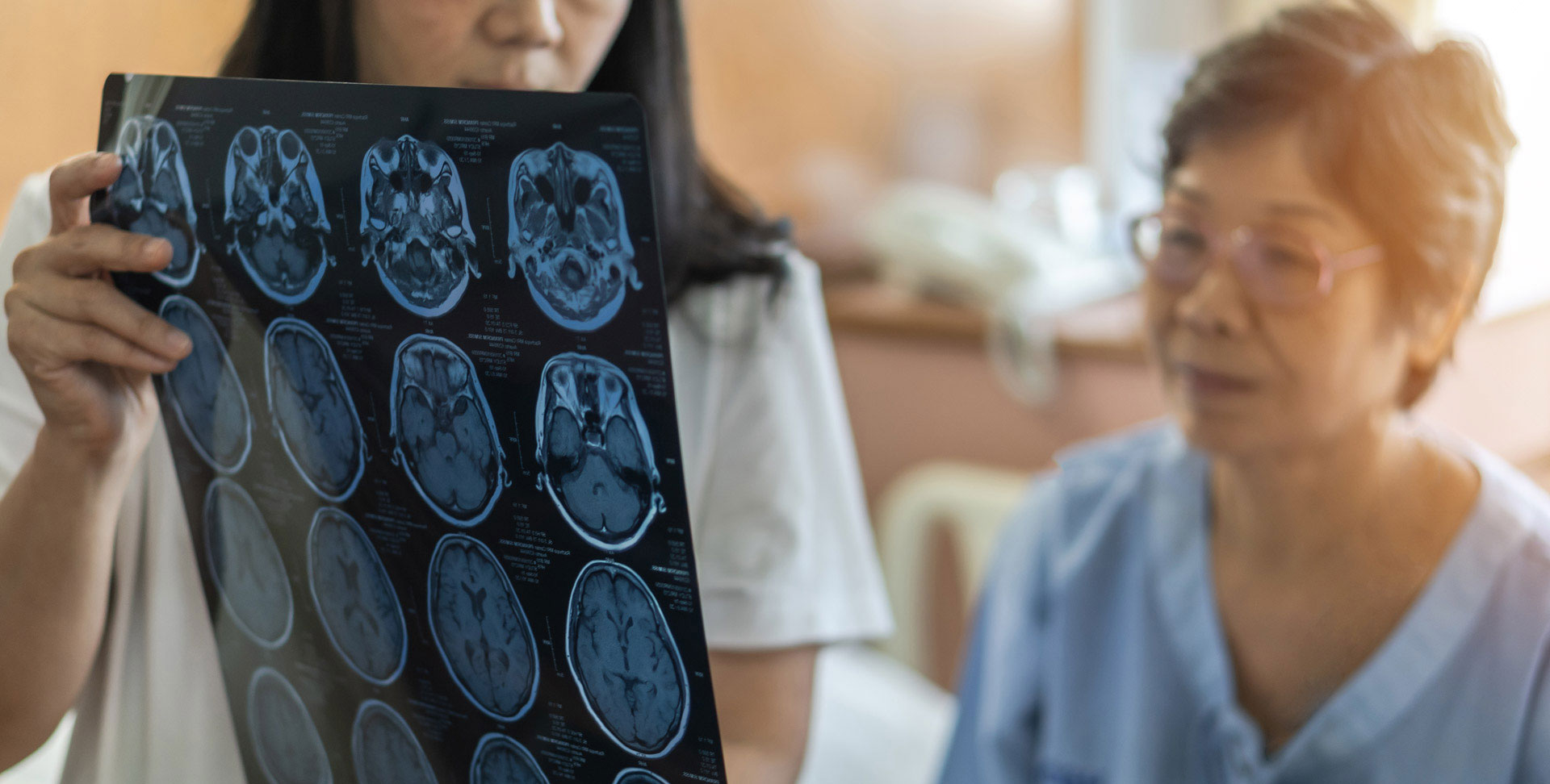 A doctor holds up a sheet of brain scans and is explaining them to her patient