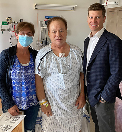 Darrell Parker beside his hospital bed next to his wife, Shirley Parker (left) and the surgeon who saved his life, Dr. Corey Adams (right).
