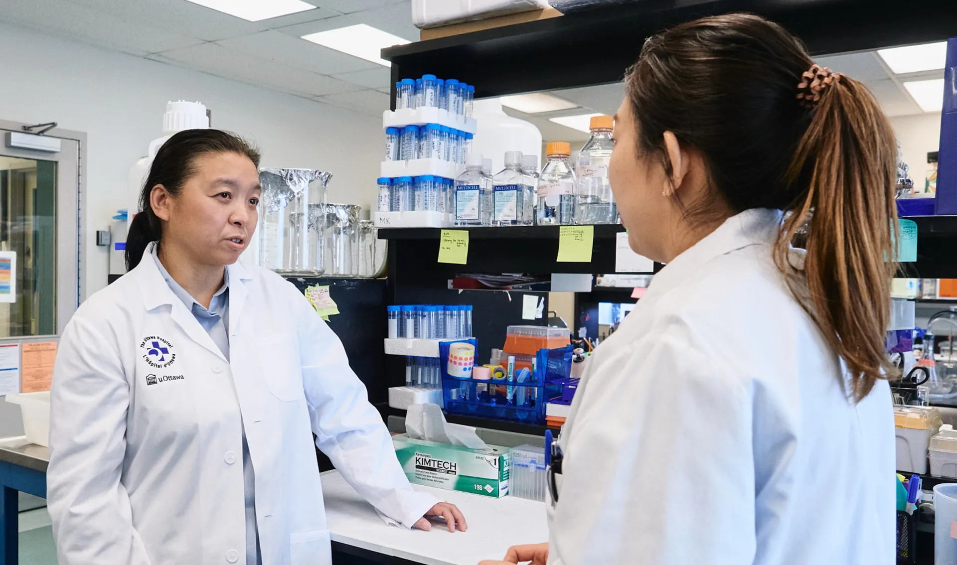 Dr. Jing Wang talking with a coworker in the laboratory.
