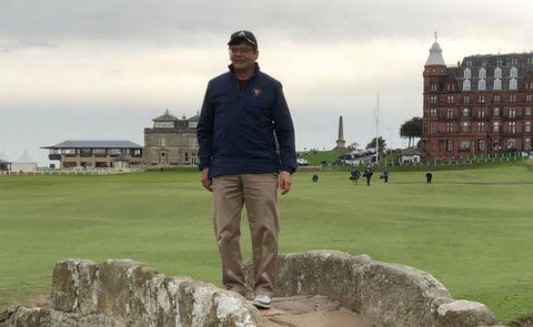 A man stands on a stone bridge on a golf course under gray skies.