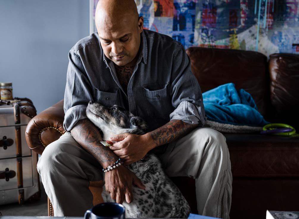 Kevin sits on a sofa and pats his dog.