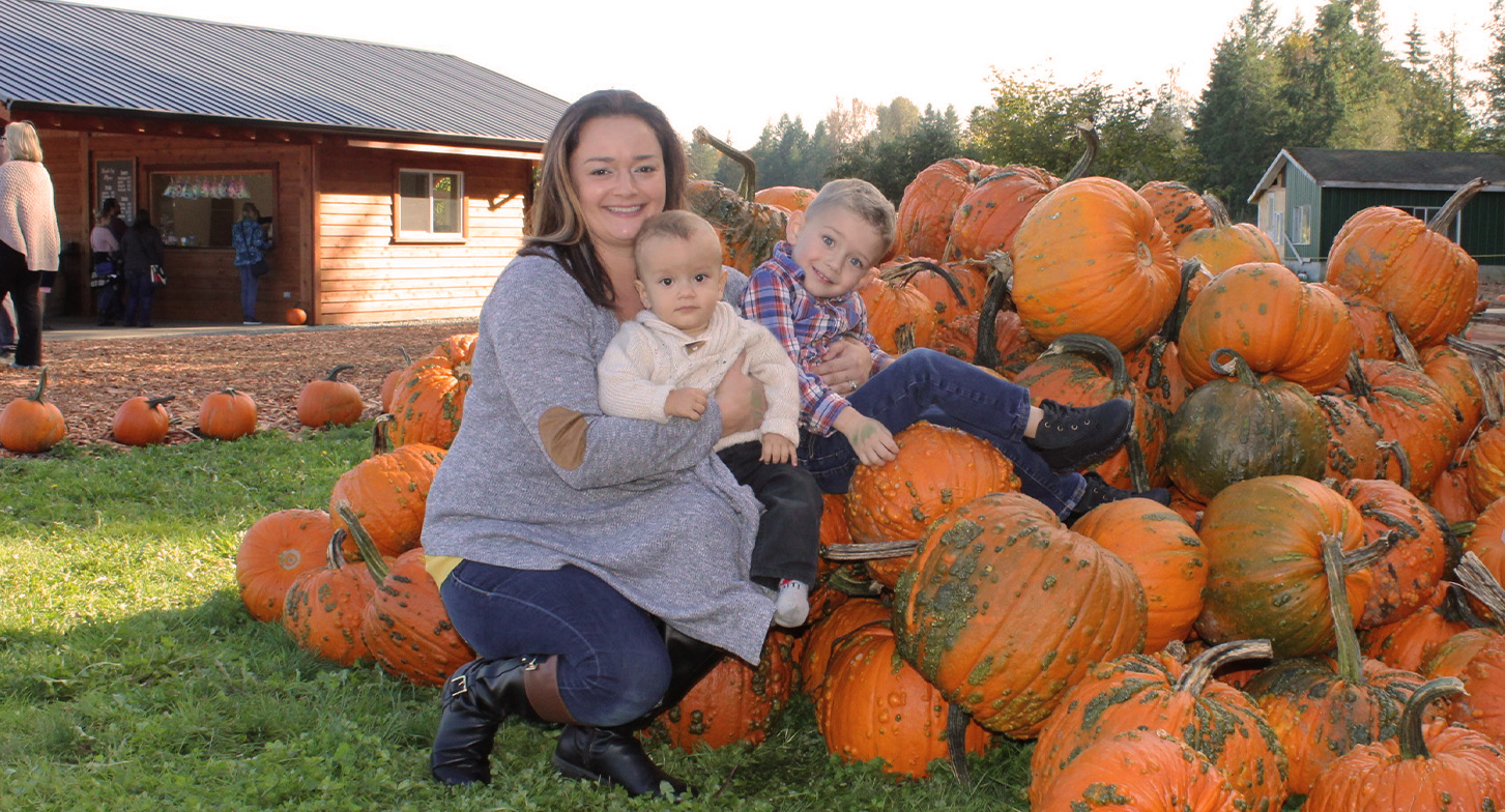 Megan with her kids Levi and Lucas beside a pile of pumpkins. 