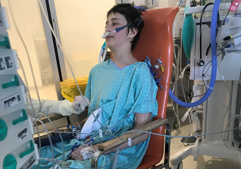 Olivier Lanthier sits in a chair wearing a hospital gown, surrounded by medical equipment.