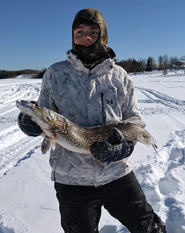 Marcus kneels in a snowy landscape holding a large fish.