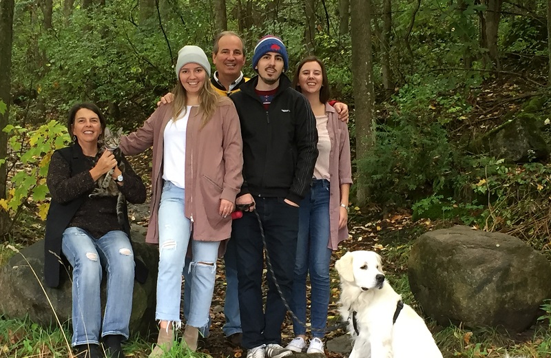 Paul King smiles with his wife and three grown children in a forest.
