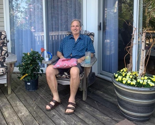 Paul King sits on a chair outdoors, with a pillow on his lap.